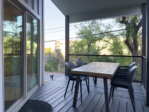 Une terrasse en bois avec une table et des chaises, donnant sur un jardin arboré et sur un bâtiment visible au loin.