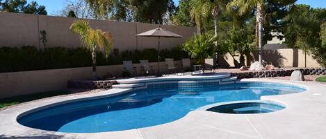 A swimming pool with a curved design, surrounded by a concrete deck and a low wall with a decorative pattern.