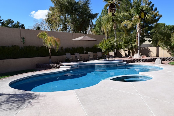 A swimming pool with a curved design, surrounded by a concrete deck and a low wall with a decorative pattern.
