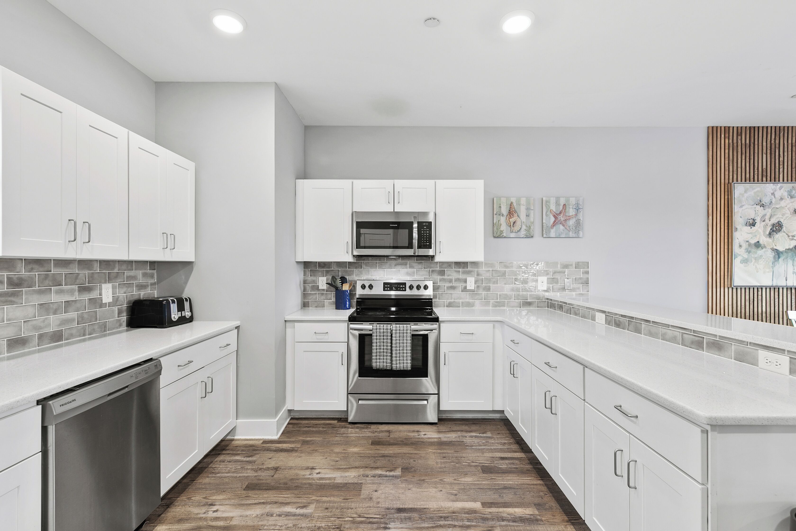Una cocina moderna con gabinetes blancos, lavavajillas de acero inoxidable, microondas y horno.