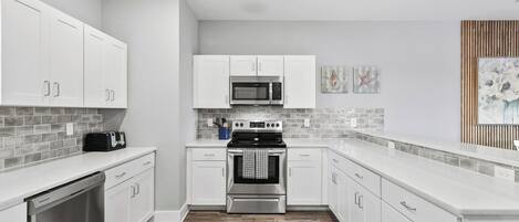 Una cocina moderna con gabinetes blancos, lavavajillas de acero inoxidable, microondas y horno.