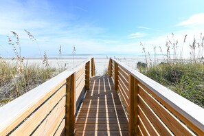 Una pasarela de madera que conduce a una playa con arena y algas.