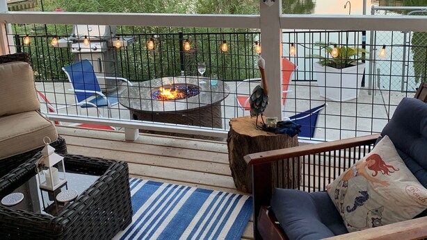 A covered outdoor deck with wicker furniture, a fire pit, and a view of a lake and hills.