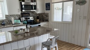 A modern kitchen with white cabinets, a granite countertop, stainless steel appliances, and two bar stools.