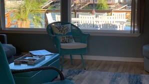 A room with a view of a lake, a wicker chair with a cushion, a small table with a tray, and a blue umbrella outside.