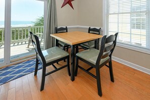 A dining area with a wooden table and four chairs, a red star decoration on the wall, and a view of the ocean through large windows.