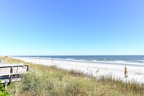 A beach with a wooden boardwalk leading to the shore, surrounded by tall grass and sand.