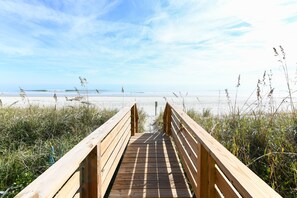 Une promenade en bois menant à une plage, avec un ciel dégagé.