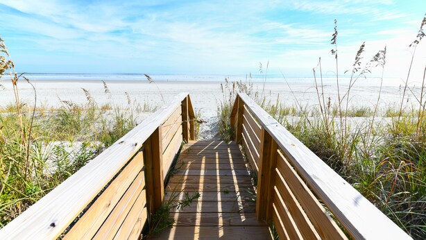 Een houten looppad dat naar een strand met zand en wier leidt.