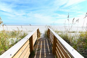 Une promenade en bois menant à une plage de sable et d’algues.