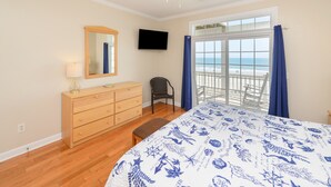 Een slaapkamer met een bed, een dressoir, een stoel, een televisie en een balkon met uitzicht op de oceaan.