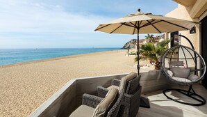 A beachside patio with wicker furniture, a hanging chair, and a large umbrella.