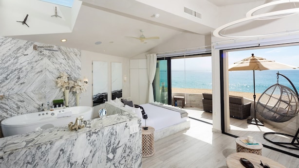 A modern bathroom with a marble vanity, a large bathtub, and a view of the sea through a glass door.
