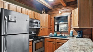 A kitchen with wooden cabinets, stainless steel appliances, granite countertops, and a window with blinds.
