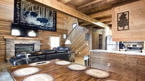 A wooden interior with a fireplace, leather sofa, dining table with placemats, kitchen area, and a staircase.