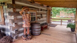 Ein rustikales Blockhaus mit einer Holzstatue, einem Fass und einer Bank auf der Veranda.