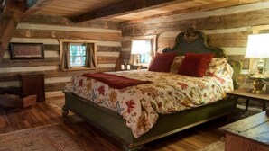 Ein Schlafzimmer einer Blockhütte mit einem Bett, zwei Fenstern, einem Nachttisch und einer Lampe.