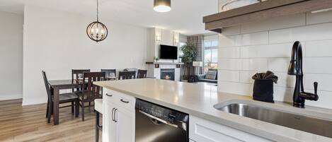 A modern kitchen with a dishwasher, a sink, and a dining area with chairs and a table.