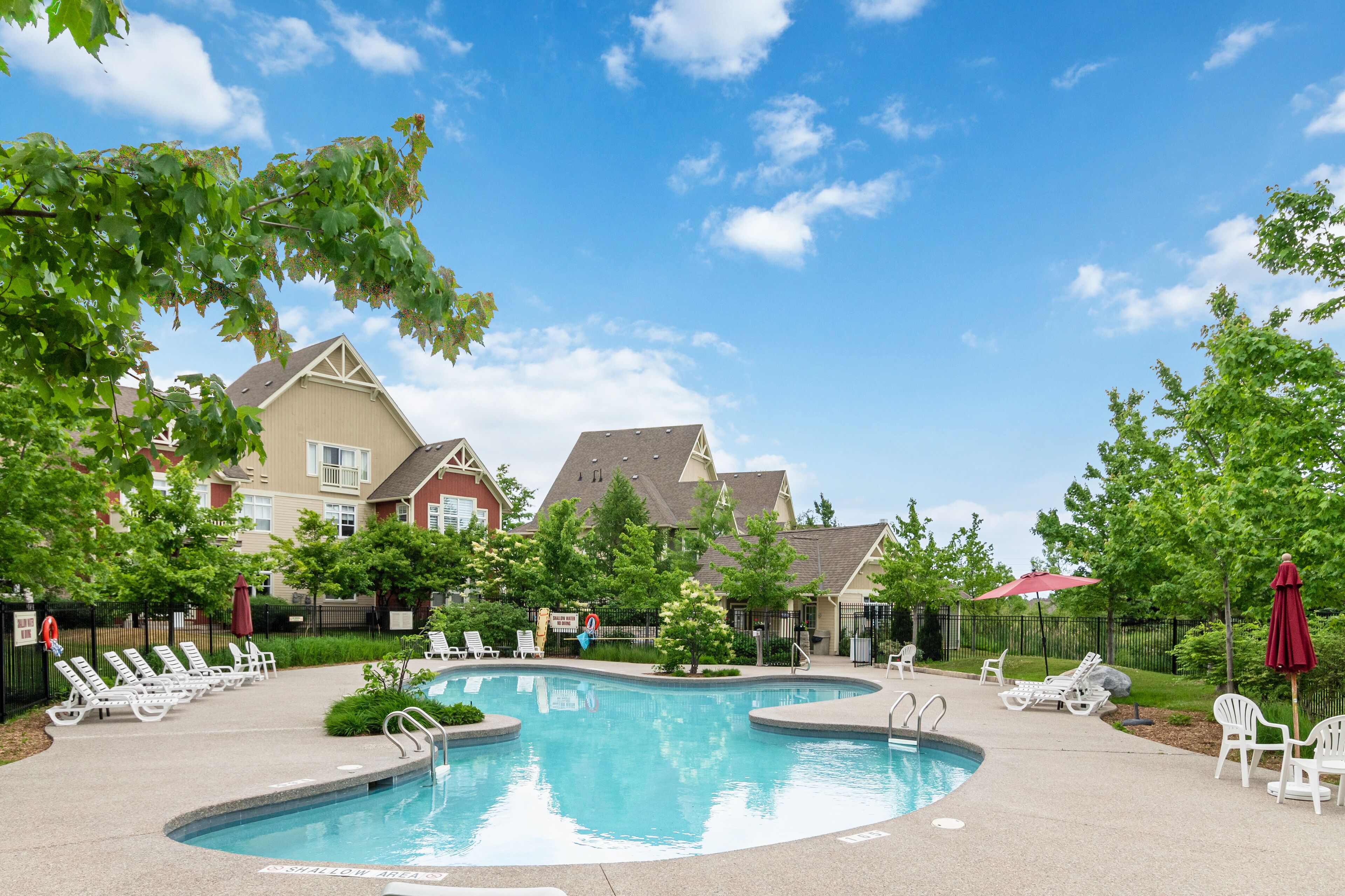 A swimming pool with lounge chairs and umbrellas, surrounded by trees and buildings.