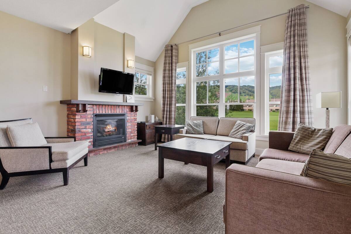A living room with a fireplace, a television, and a large window with curtains.