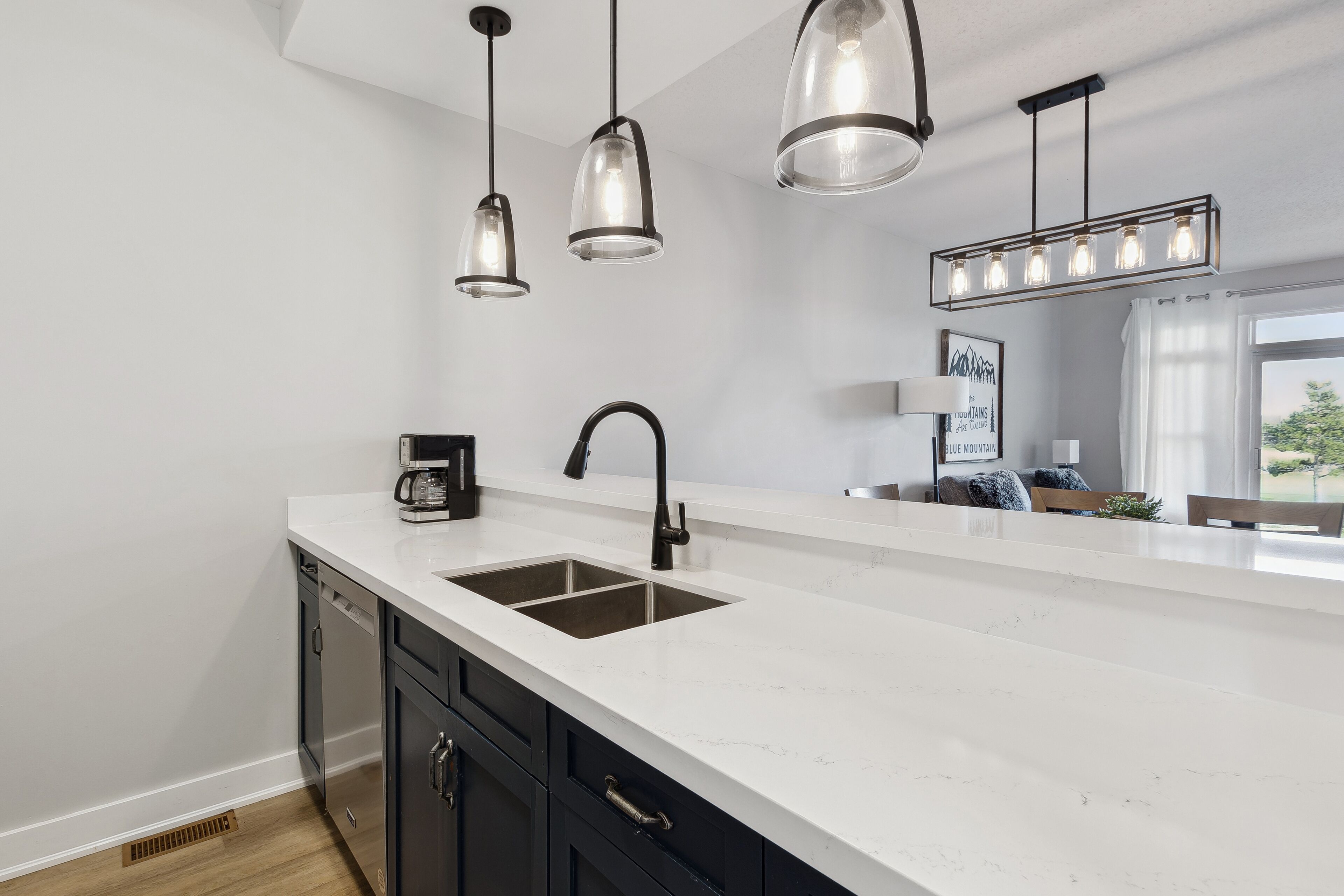 A modern kitchen with a white countertop, black cabinets, a double sink, and pendant lighting.