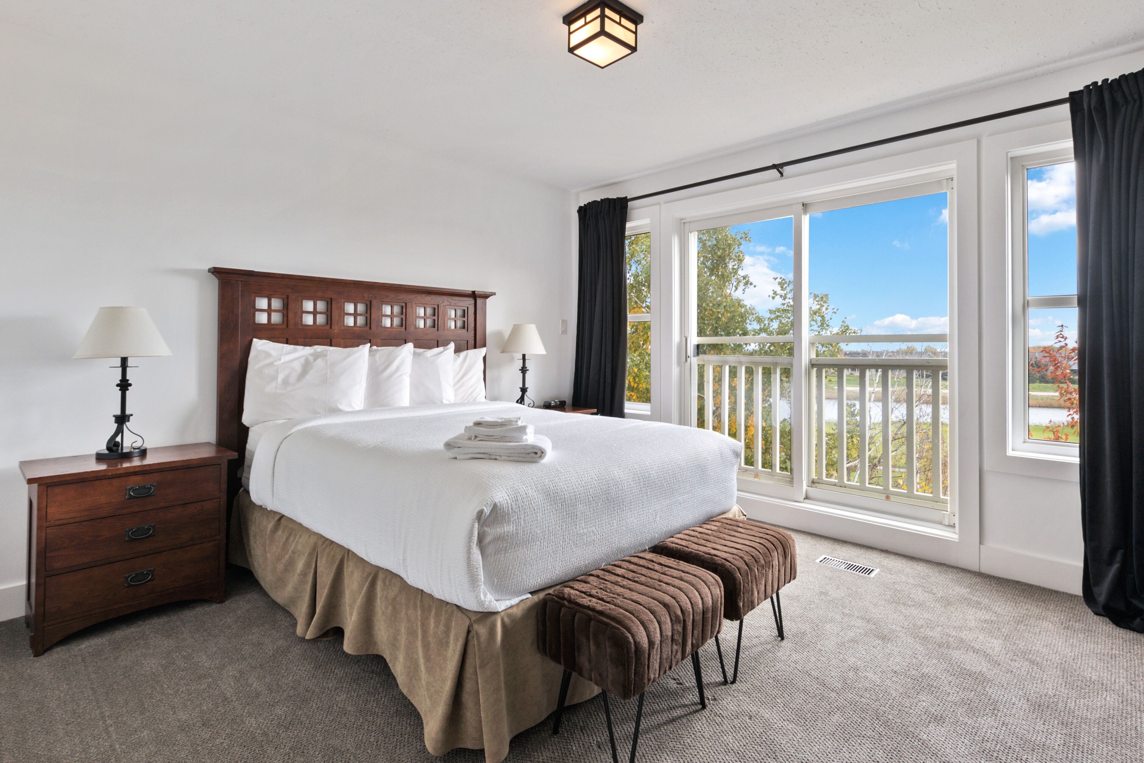 A hotel room with a large bed, two bedside tables, a bench, and a balcony with a railing.