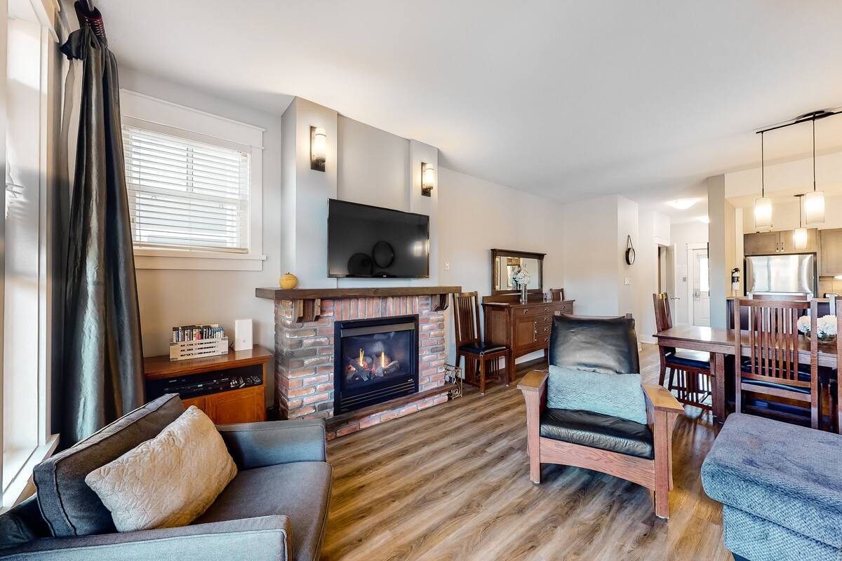 A living room with a fireplace, a television mounted above it, and a dining area with wooden furniture.