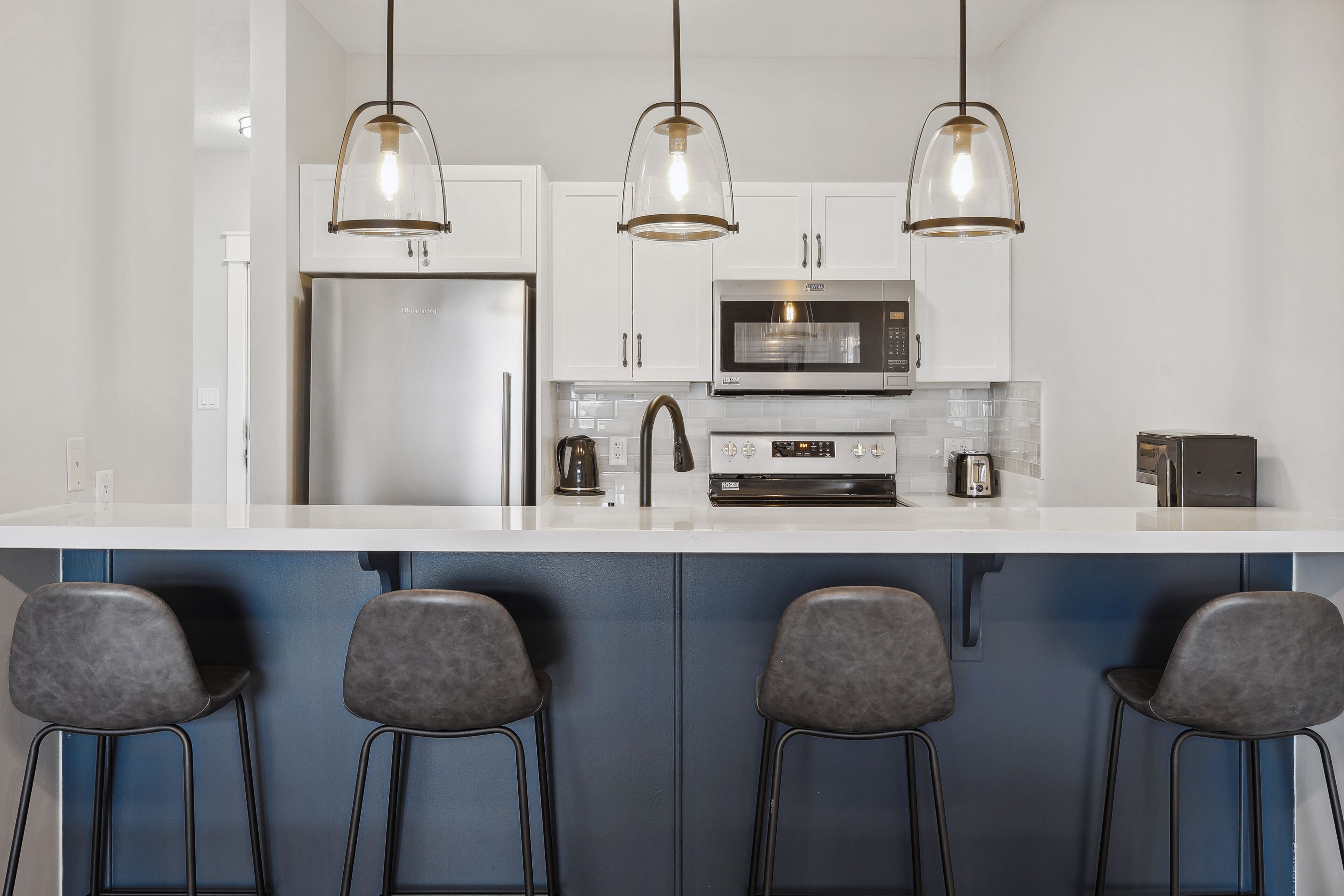 A modern kitchen with a large island, stainless steel appliances, and bar stools.