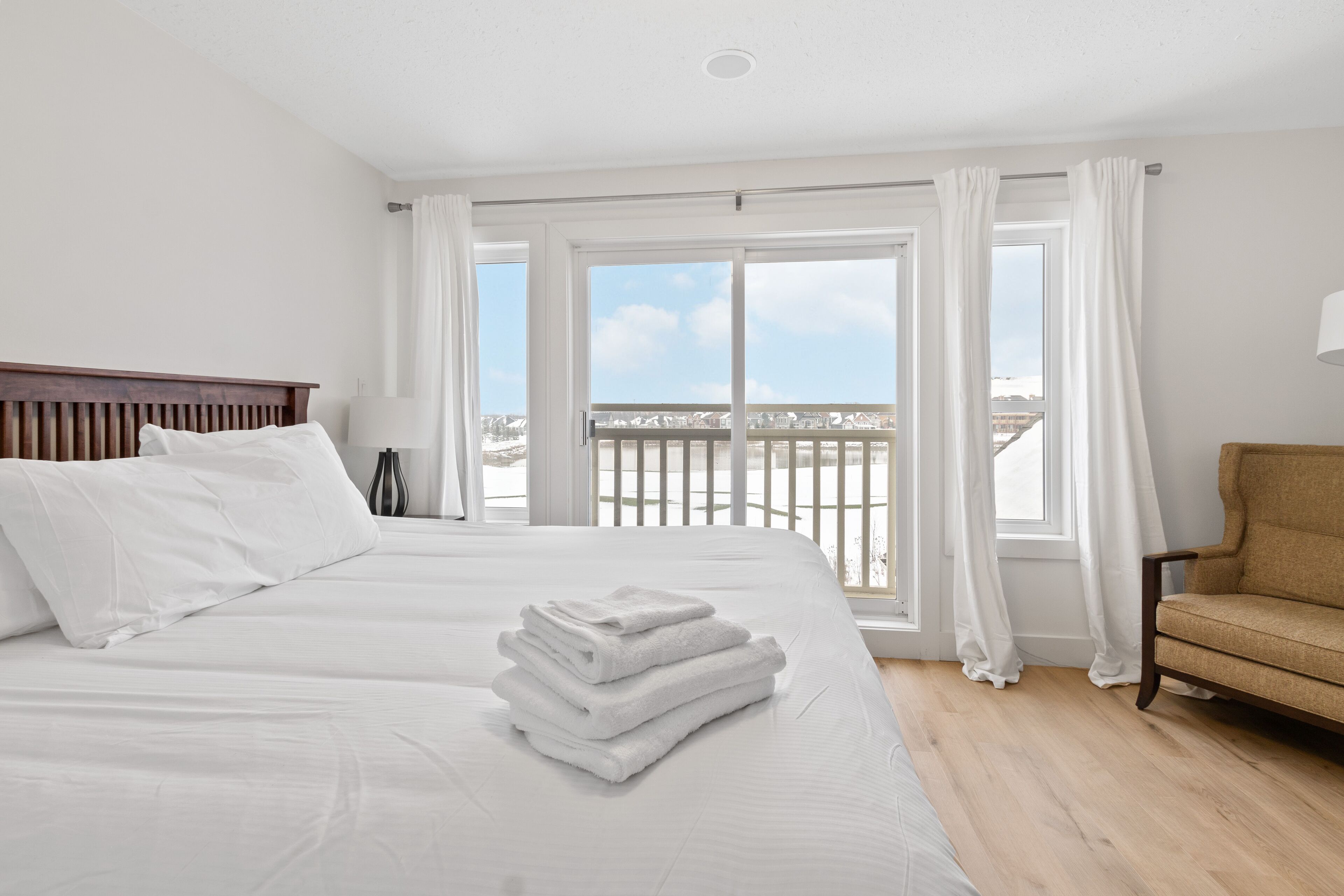 A hotel room with a large bed, a chair, and a view of the sea through the windows.