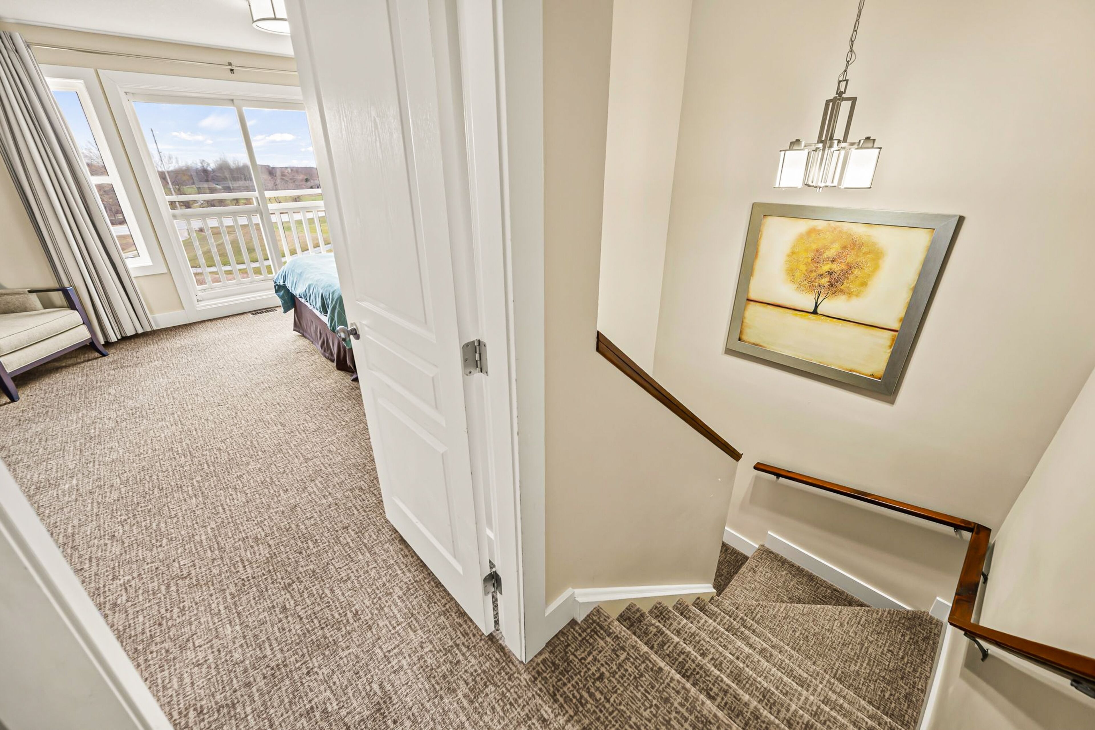 A hotel room with a large sliding glass door leading to a balcony, a framed artwork on the wall, and a carpeted floor.