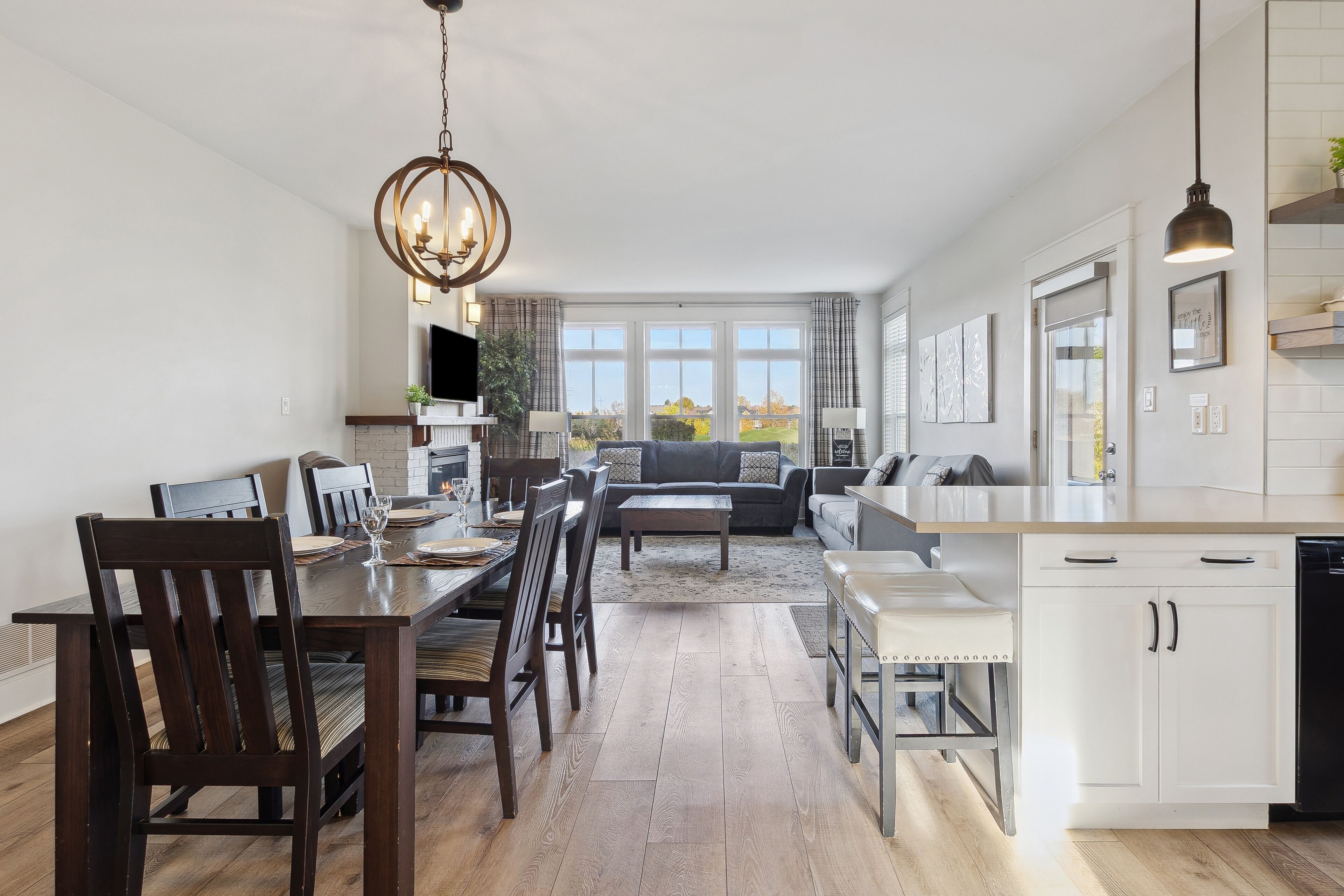 A modern kitchen with white cabinetry, a dining area with wooden chairs, and a large window offering a view of the outdoors.