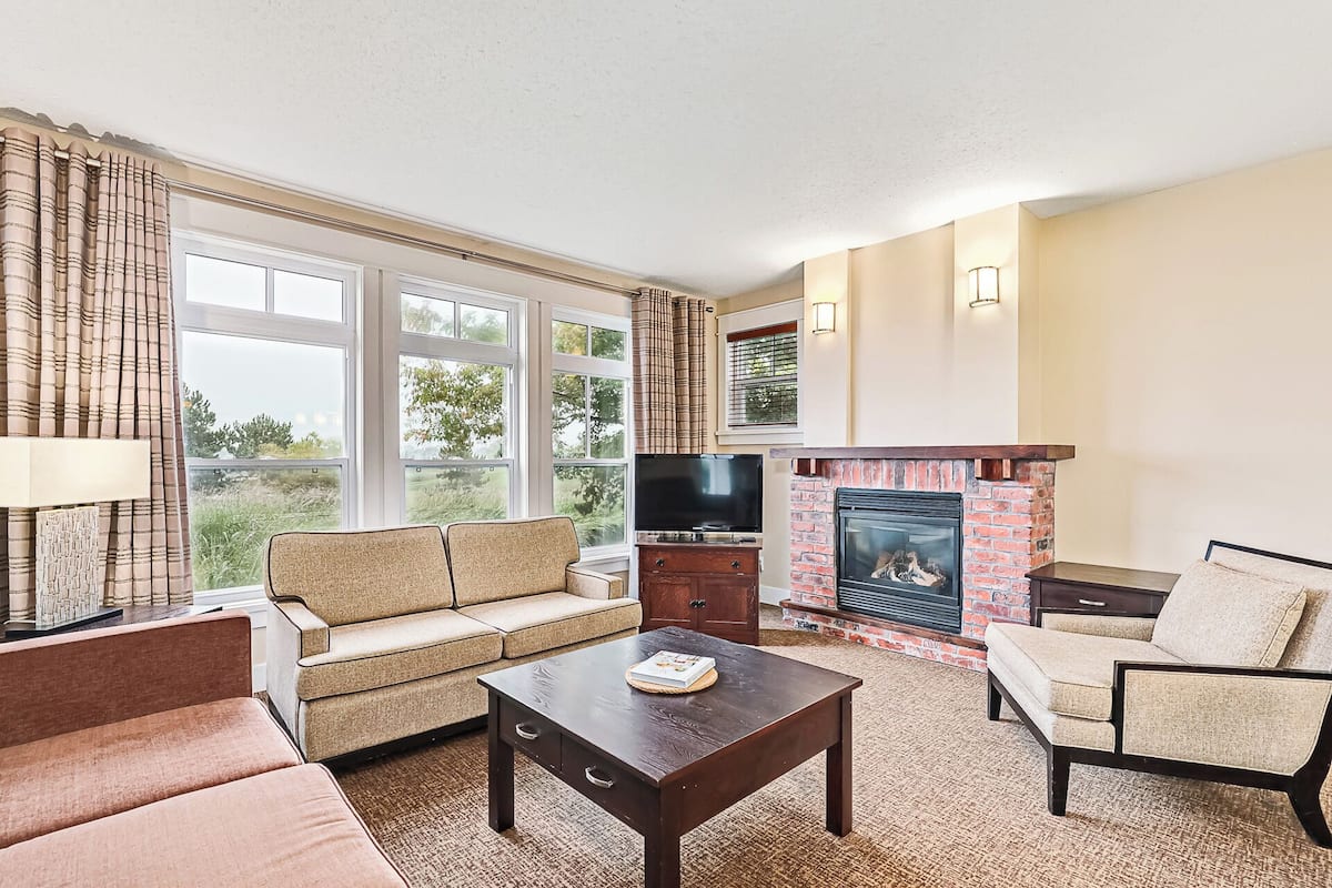 A living room with a sofa, armchairs, a coffee table, a fireplace, and a television.