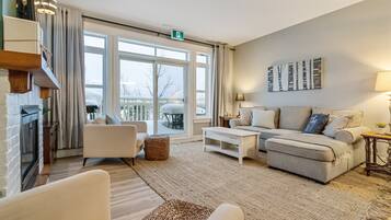 A modern living room with a fireplace, a sofa set, and a large window offering a view of the outdoors.