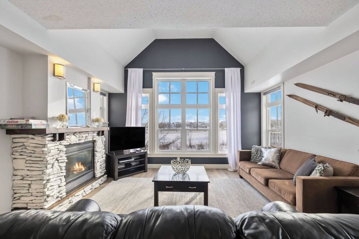A living room with a stone fireplace, a television, a sofa, and a large window with curtains.