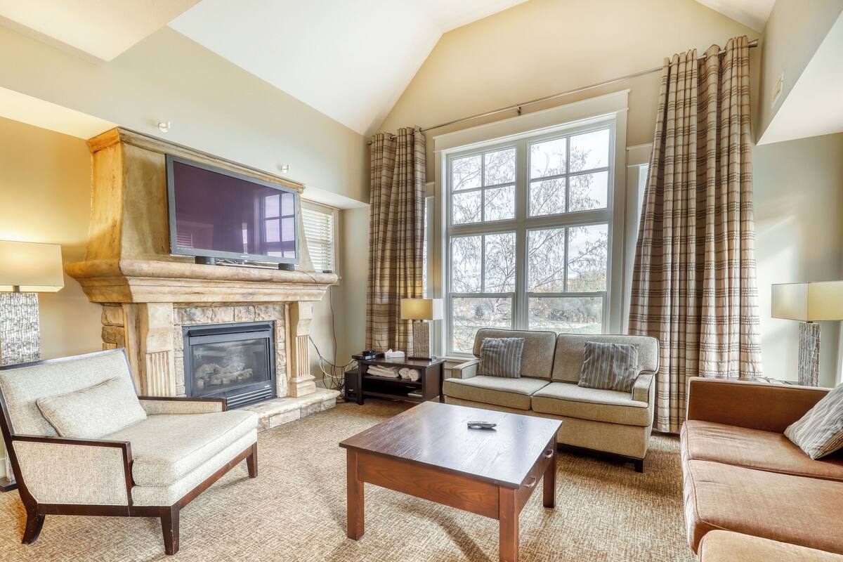 A living room with a fireplace, a television, and a large window with curtains.