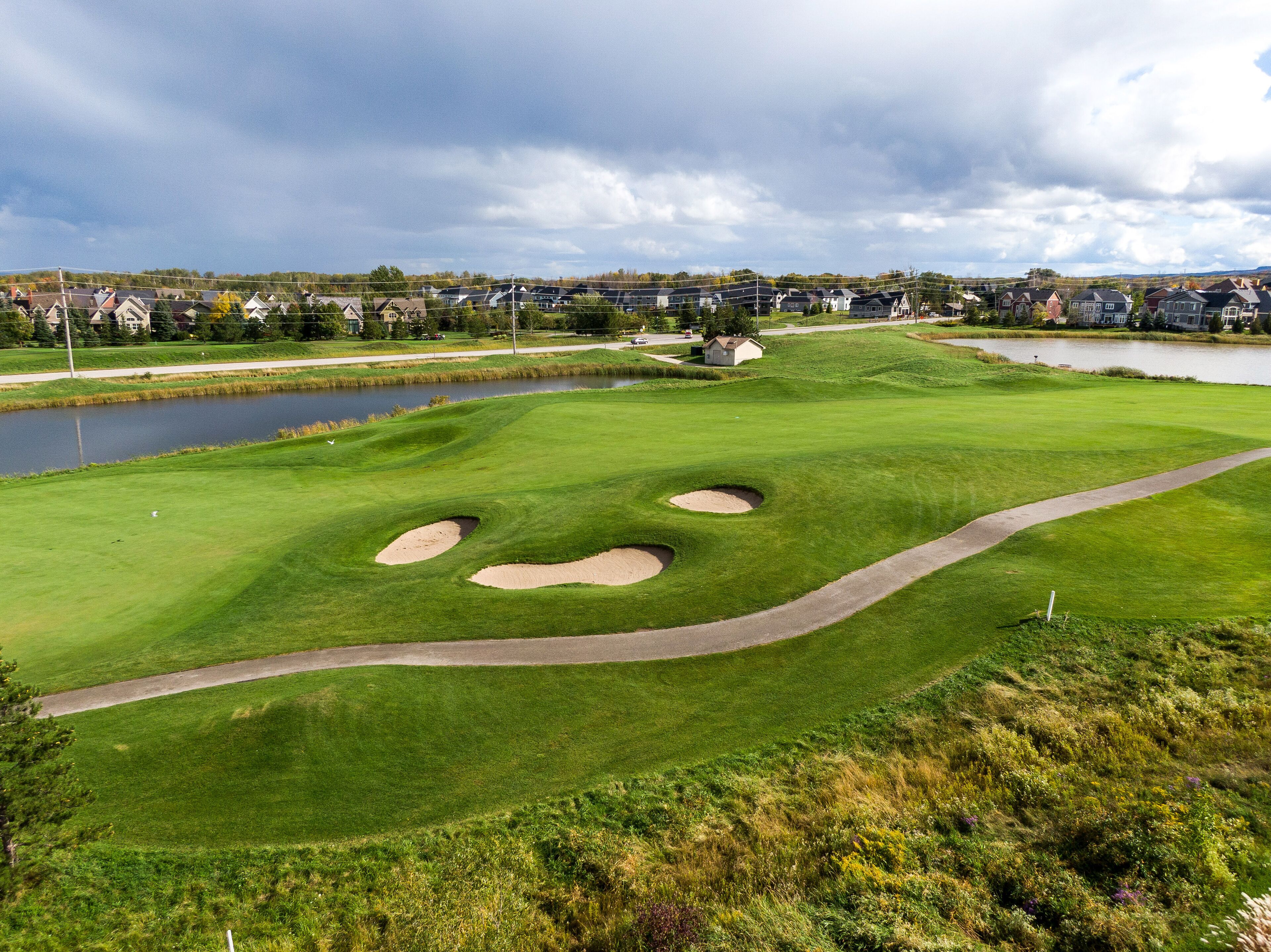A golf course with bunkers, a pond, and houses in the background.