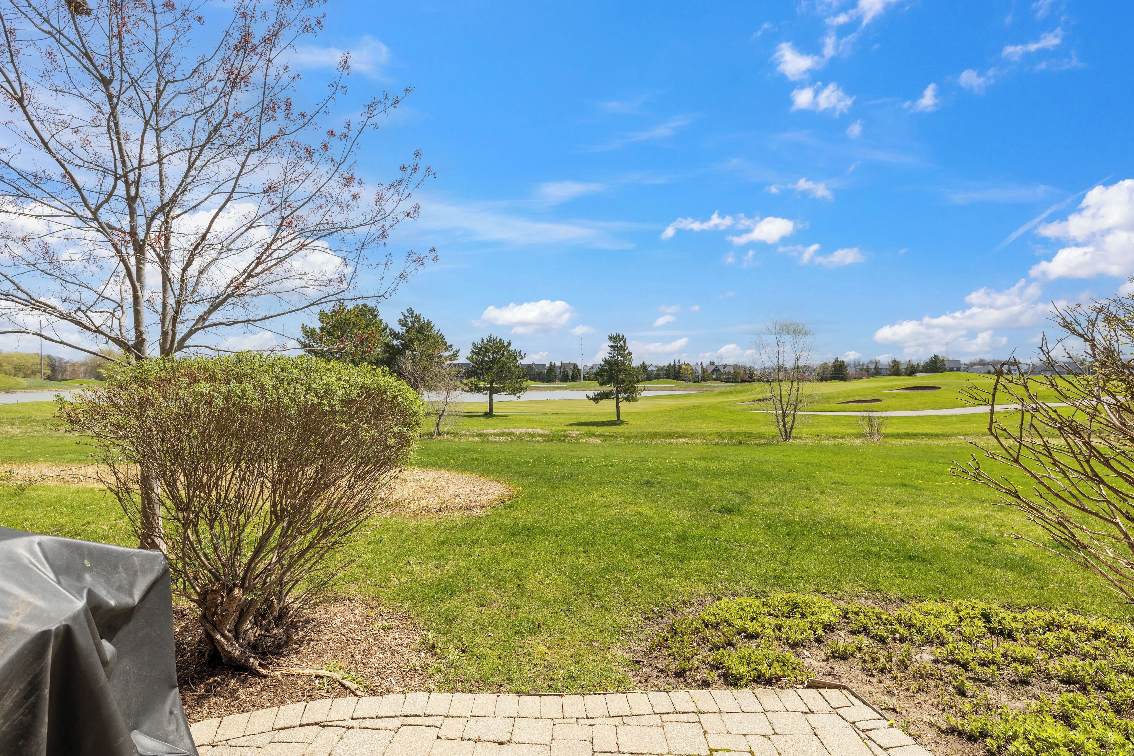A golf course with a clear sky, a paved walkway, and a covered seating area.