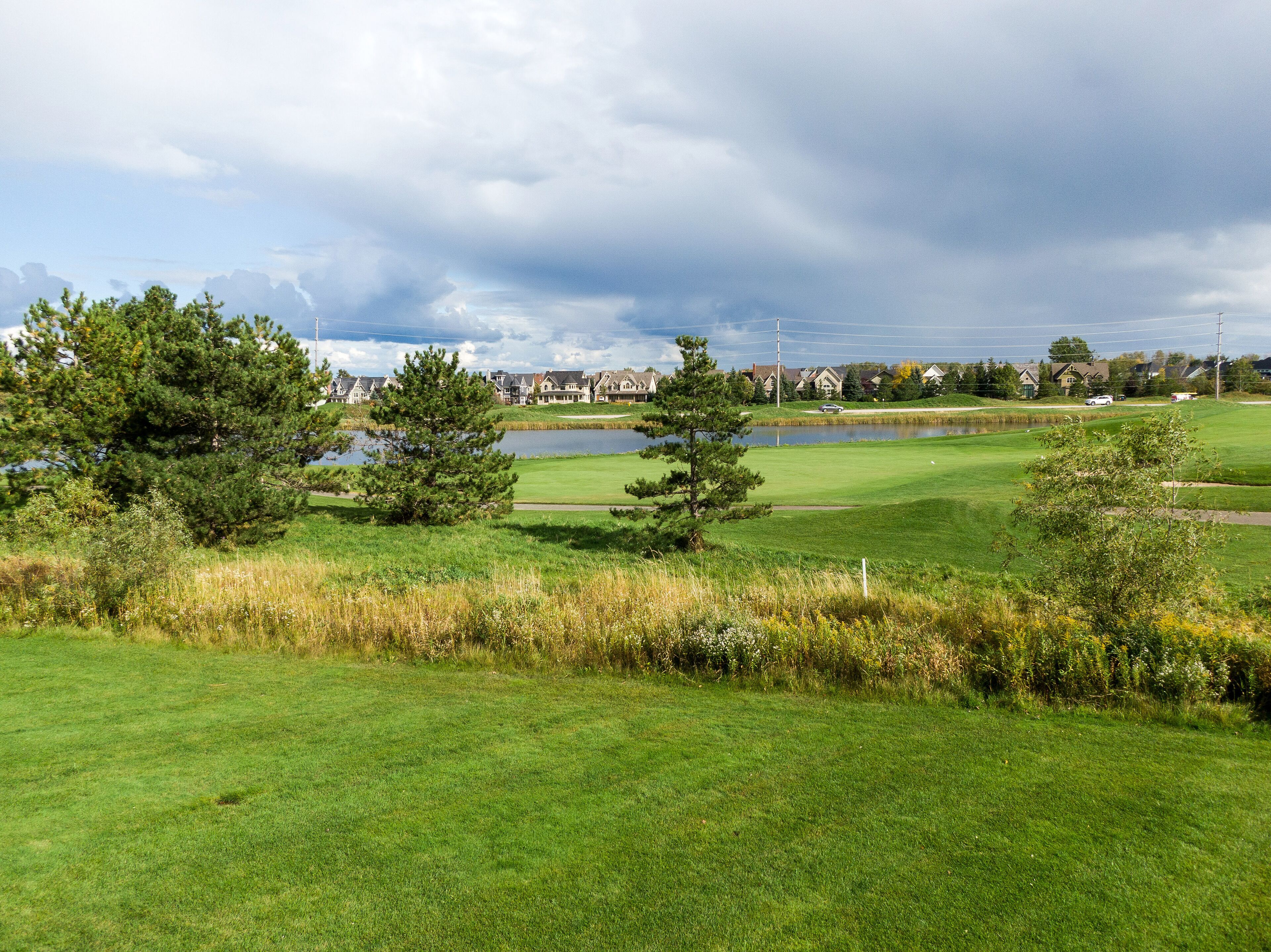 Un parcours de golf avec un étang, des arbres et des maisons en arrière-plan.