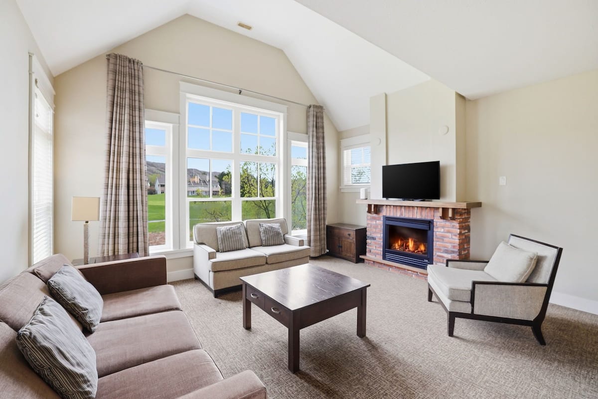A spacious living room with a fireplace, a sofa, a chair, and a television.