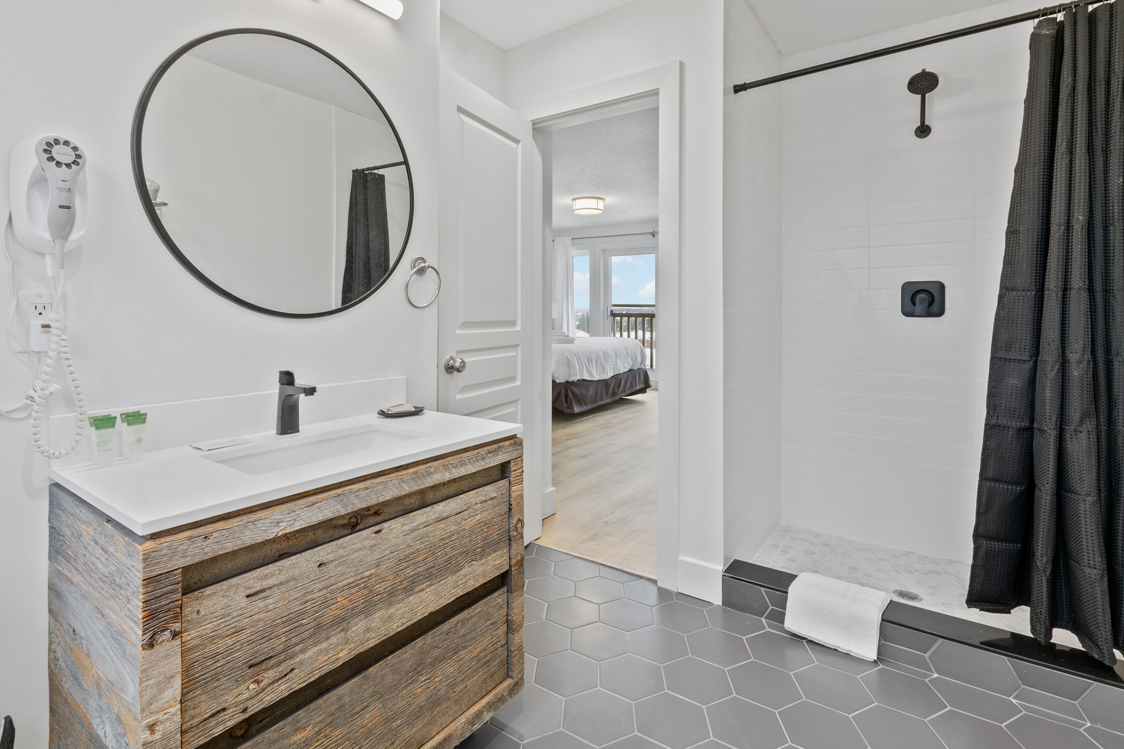 A modern bathroom with a white vanity, a round mirror, and a shower area.