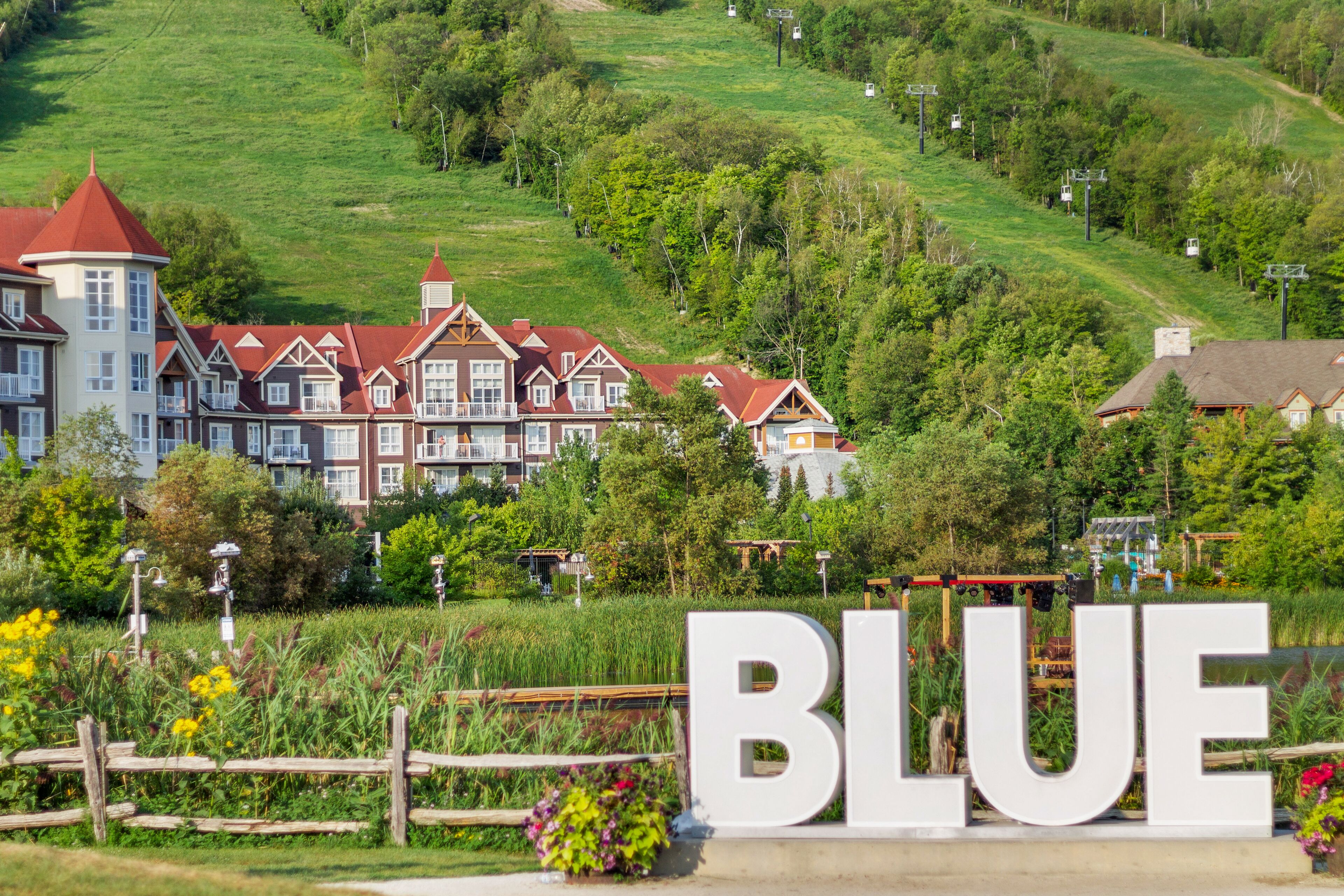A large, historic building with multiple red roofs and white walls, surrounded by lush greenery and a sign that reads "BLUE".