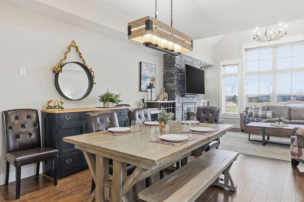 A dining area with a wooden table, chairs, and a bench. There is a TV mounted on the wall and a fireplace.