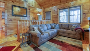 A cozy cabin interior with a wooden floor, a sectional sofa, a small table, and a large window with blinds. - Couples Getaway! Private, Romantic, Cabin with Jacuzzi & Hot Tub in Gatlinburg (Gatlinburg)