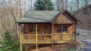 A wooden cabin with a porch, surrounded by trees. - Couples Getaway! Private, Romantic, Cabin with Jacuzzi & Hot Tub in Gatlinburg (Gatlinburg)