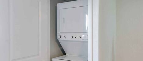 A laundry room with a front-loading washer and dryer stacked vertically.
