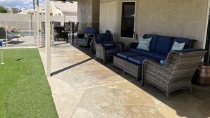 Ein überdachter Patio-Bereich mit Korbmöbeln, einem Pool und Steinböden.