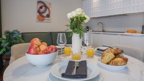 Une table mise pour le petit-déjeuner, avec un bol de fruits, des croissants et un jus d’orange, et une cuisine en arrière-plan.