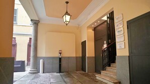 Un hall d’hôtel avec un sol en pierre, une grande colonne, un escalier et une porte ornée de panneaux indicateurs.