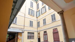 Une cour avec des murs jaunes, de nombreuses fenêtres dotées de volets et une colonne centrale.