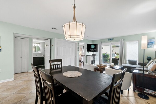 A dining area with a dark wooden table, white chairs, and a central light fixture.